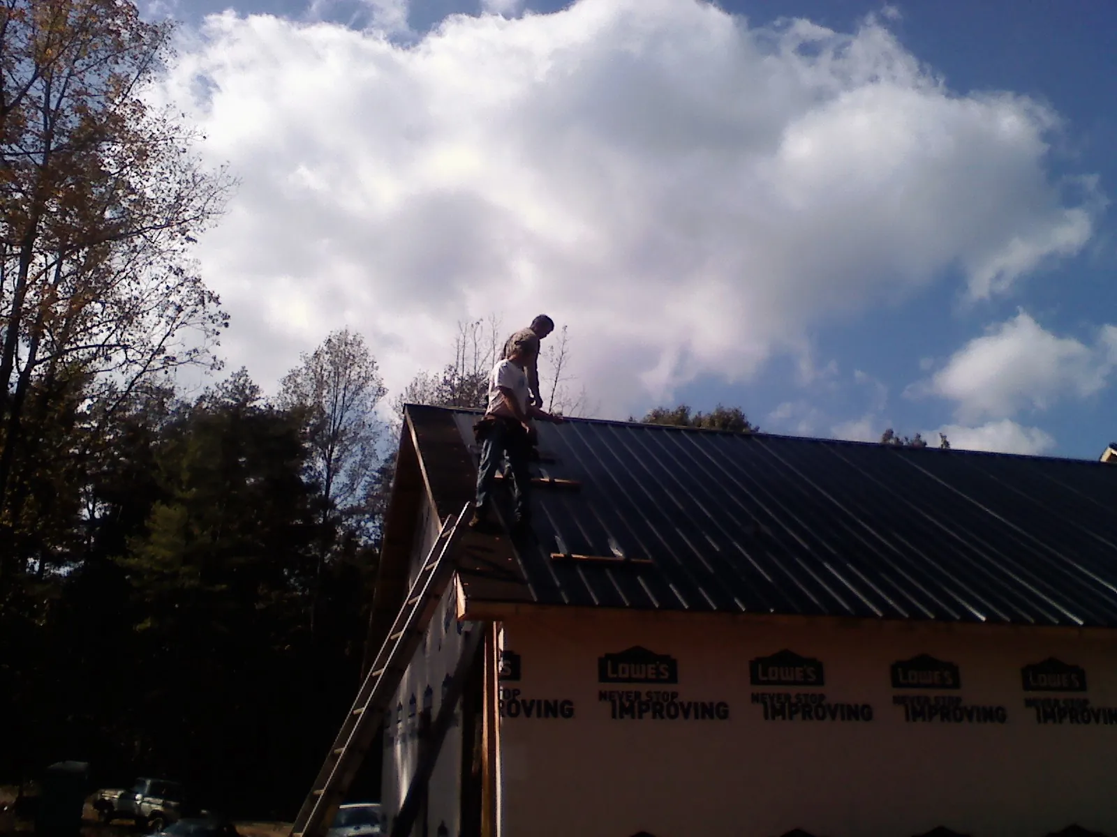 Roofer fastening dark metal panels high against a cloudy sky, from a Roof Inspection job in Barrington
